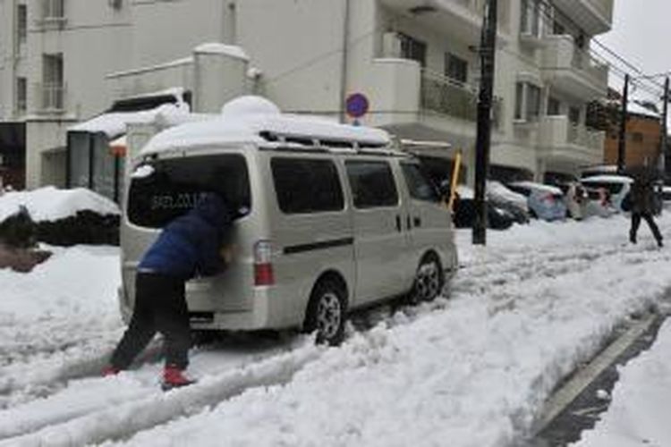 Seorang pria terpaksa mendorong mobilnya yang selip akibat tumpukan salju tebal menutupi ruas-ruas jalan di kota Tokyo, Jepang, Sabtu (15/2/2014). Di seluruh Jepang, badai salju hebat yang menghantam negeri itu menewaskan sedikitnya 11 orang.