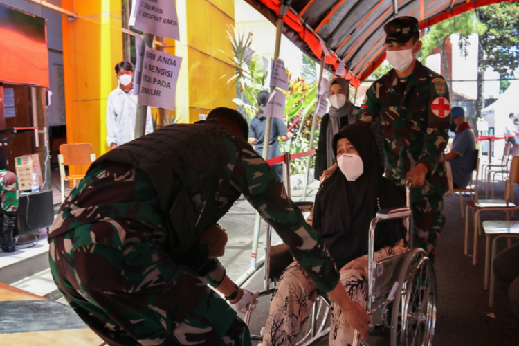 Anggota Kodam III/Siliwangi membantu seorang wanita yang memakai kursi roda untuk ikut proses vaksinasi di Itenas.