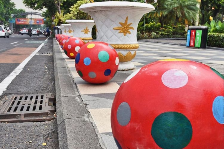 Ilustrasi benda berbentuk bola di trotoar jalan.