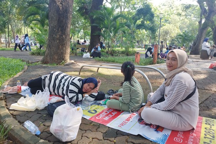 Eci (53) dan keluarganya beristirahat di kawasan Monas, Jakarta Pusat, Kamis (11/4/2024).
