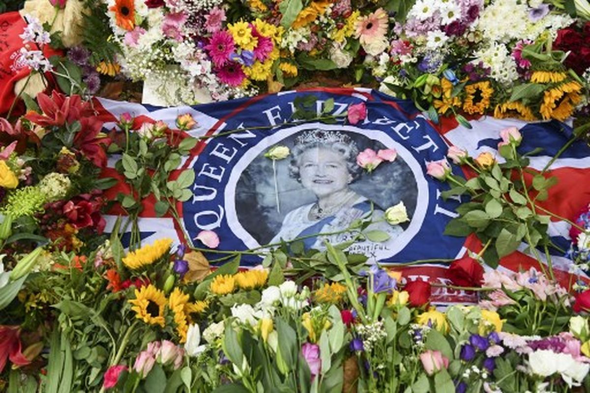 Sebuah bendera dengan gambar Ratu Inggris Elizabeth II terlihat di antara bunga yang ditempatkan oleh simpatisan di dekat Istana Buckingham di London pada 11 September 2022. 