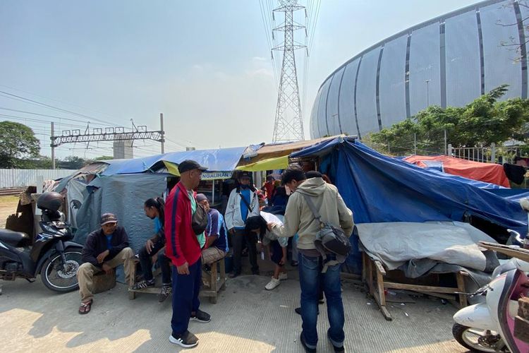 Warga Kampung Bayam tengah berkumpul di depan tendanya karena mendapatkan kabar bahwa tempat tinggal sementaranya itu akan segera dibongkar oleh pihak Kelurahan Papanggo.  