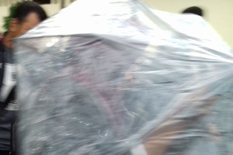 Plt Kepala Dinas Kesehatan Kabupaten Malang, Ratih Maharani saat menutup diri dari payung usai diperiksa sebagai saksi oleh penyidik KPK di Mapolres Malang Kota, Rabu (28/11/2018)