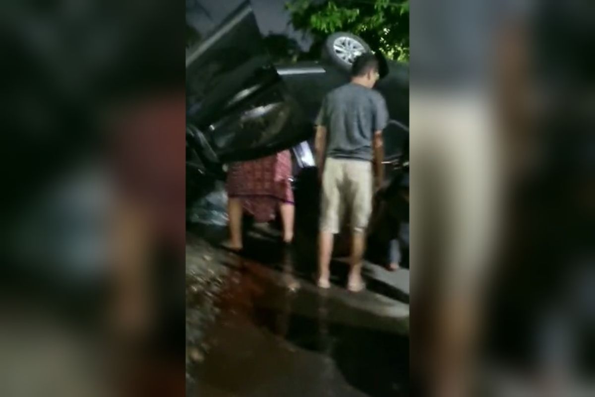 Warga yang mulai berdatangan melihat kondisi mobil dan pengemudinya usai menabrak tiang listrik hingga terguling di bilangan Jalan Cendrawasih, Kota Makassar, Sulawesi Selatan (Sulsel). Sabtu (29/4/2023)