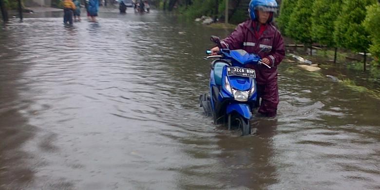 Salah satu pengendara terpaksa menuntun motornya lantaran banjir yang menggenangi jalan Peternakan II, Kapuk, Jakarta Barat, Senin (9/2/2015)
