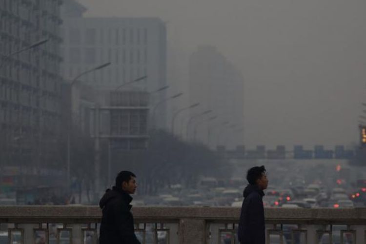 Lalu lintas bergerak sepanjang jalan sebagai pejalan kaki berjalan di sebuah jembatan diselimuti kabut di Beijing, Cina.