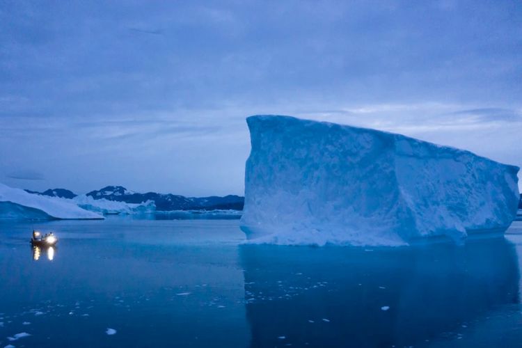 Sebuah kapal yang berlayar pada malam hari, bergerak melewati bongkahan es besar di wilayah timur Greenland pada 15 Agustus 2019.