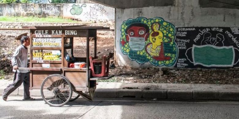 Pedagang kaki lima berjalan di dekat mural bertema pencegahaan penyebaran virus Corona atau COVID-19 di Jakarta, Rabu (01/04) 