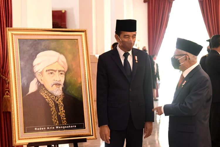 Presiden Joko Widodo berbincang dengan Wakil Presiden Ma?ruf Amin di depan lukisan Raden Aria Wangsakara, Pahlawan Nasional dari Banten yang dianugerahkan pada Rabu (10/11/2021). 
