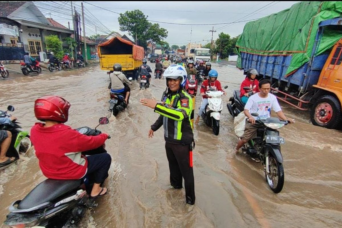 Petugas kepolisian dai Satlantas Polres Pasuruan Kota membantu pengguna jalan raya pantura di Desa Tambakrejo Kota Pasuruan yang dilanda banjir, Selasa (21/01/2025) 