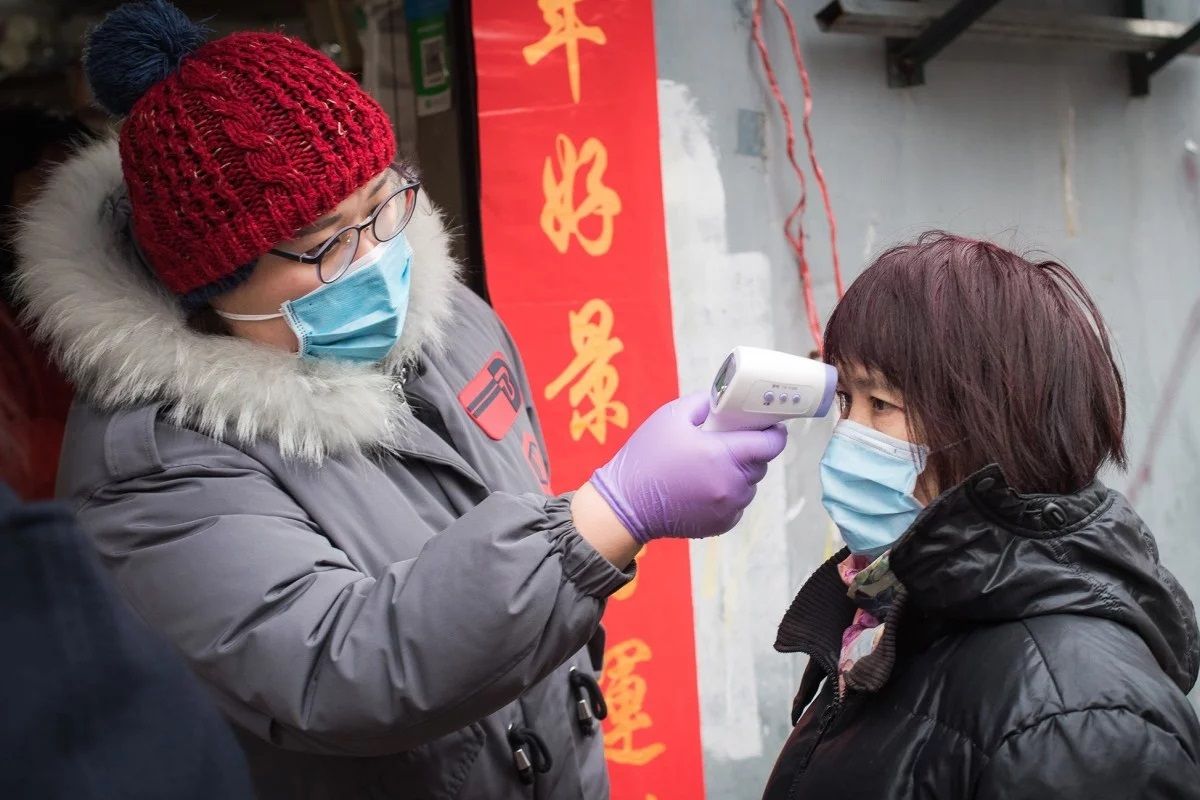 Seorang relawan komunitas mengecek suhu tubuh seorang perempuan di Paviliun Yellow Crane di Wuhan, China, pada Jumat (7/2/2020). Wabah virus corona yang mewabah di China sejak Desember 2019 dilaporkan telah membunuh 722 orang.