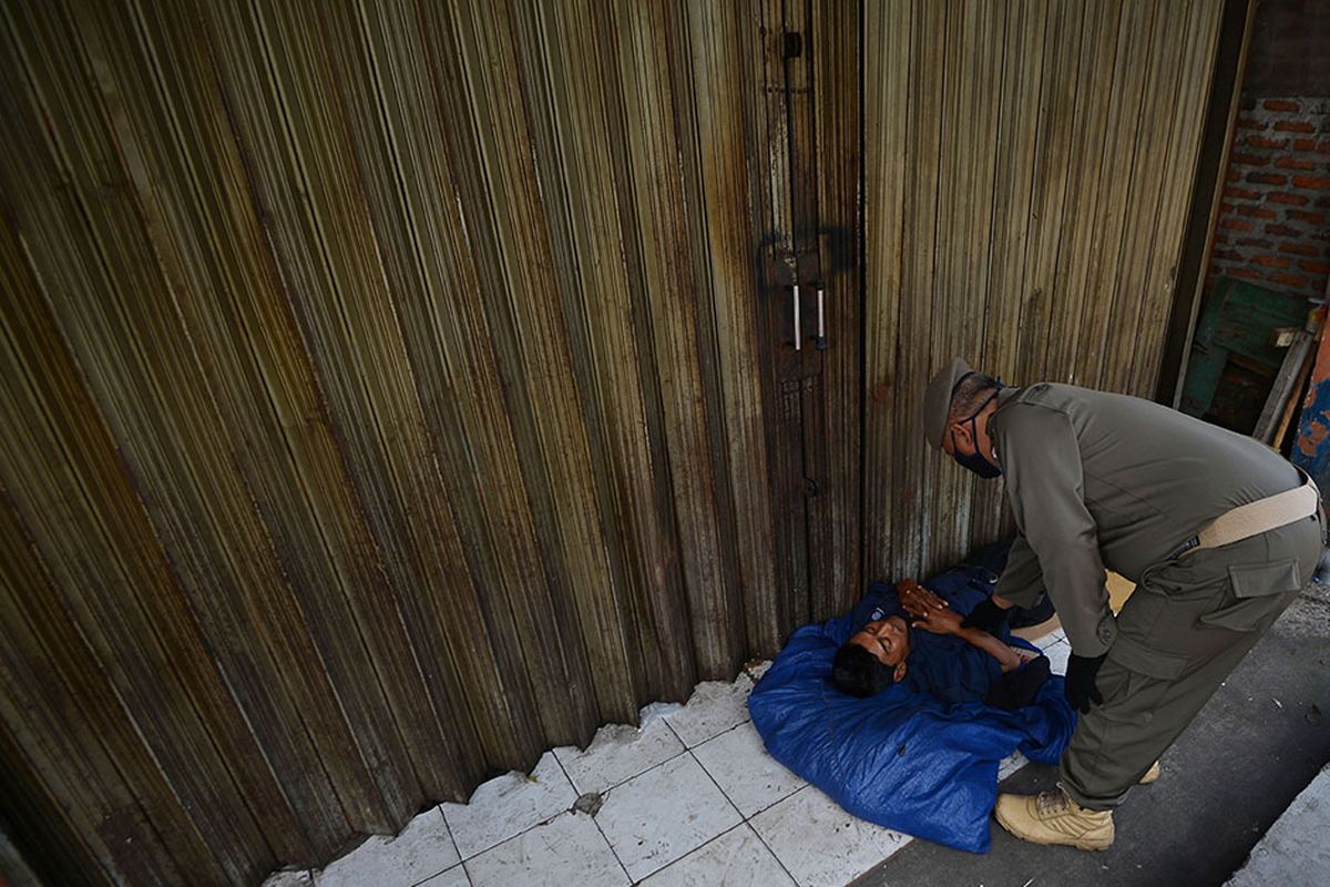 Petugas Satpol PP membangunkan seorang penyandang masalah kesejahteraan sosial (PMKS) yang tidur di emperan toko di Jalan Dewi Sartika, Cawang, Jakarta, Rabu (29/4/2020). Pemerintah Provinsi DKI Jakarta menggalakkan penertiban PMKS yang berkeliaran saat penerapan pembatasan sosial berskala besar (PSBB) untuk mencegah penyebaran COVID-19.