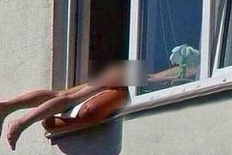 Seorang perempuan tanpa busana berjemur di jendela apartemennya.