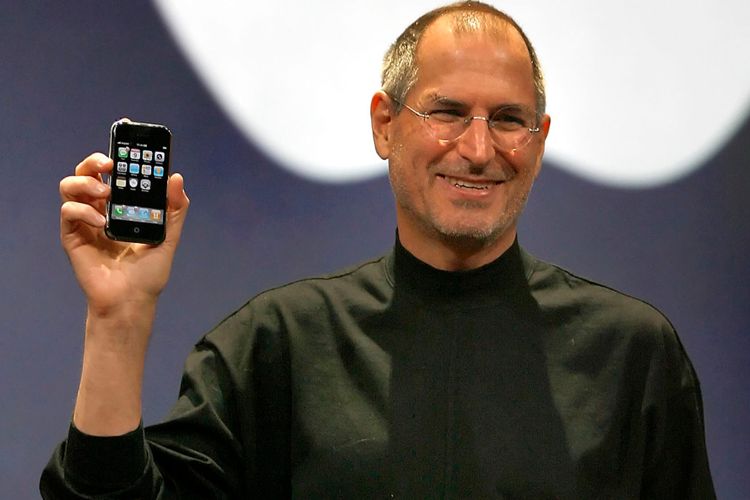 Steve Jobs memegang iPhone generasi pertama.