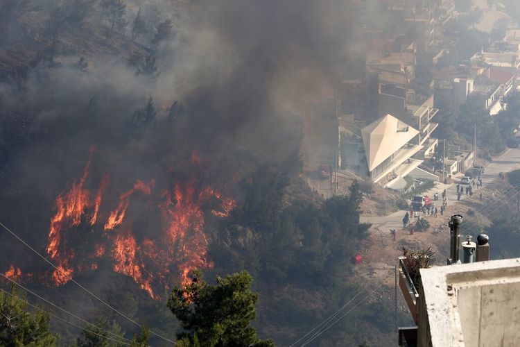 Api membakar pohon di atas bukit saat orang-orang menyaksikan kebakaran hutan di pinggiran kota Voula, di selatan Athena, Yunani, Sabtu, 4 Juni 2022.