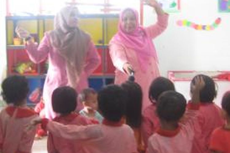 Dua orang pendidik TK mengajari anak didiknya bernyanyi untuk melatih keberanian sang anak.