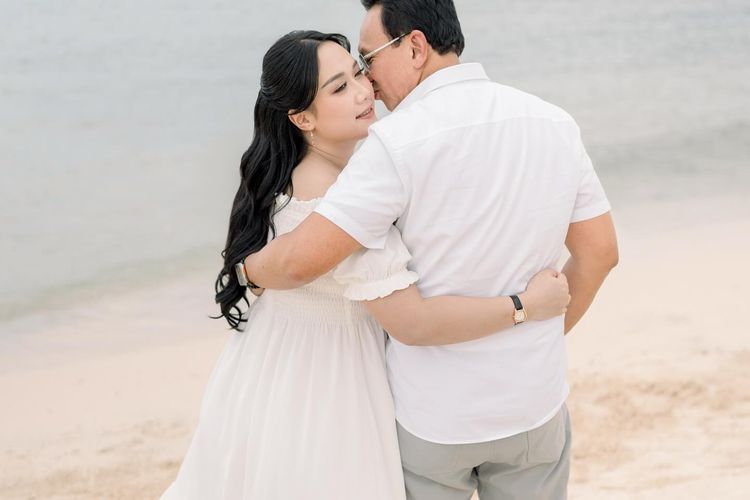 Puput Nastiti Devi tampil anggun dengan long dress putih, makeup natural, dan rambut wavy saat foto kehamilan anak ketiga bersama keluarga.