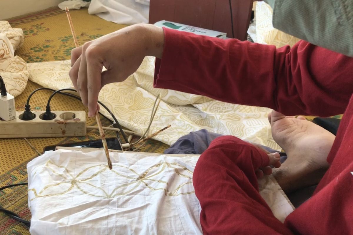 Penyandang disabilitas tuna daksa sekaligus anggota Sanggar Inspirasi Karya Inovasi Difabel (Sriekandi Patra) Darmawan Fadli Abdul Syukur (19) atau akrab disapa Wawan memegang kuas untuk mewarnai batik tulis buatannya di workshop di wilayah Dukuh Penjalinan, Desa Tawangsari, Boyolali, Jawa Tengah pada Rabu (26/7/2023). Sriekandi Patra merupakan sanggar binaan PT. Pertamina Terminal BBM Boyolali untuk membuka jalan para difabel untuk berkarya lewat batik. PT. Pertamina Terminal BBM Boyolali menghadirkan program Difablepreneur lewat Sriekandi Patra untuk meningkatkan taraf hidup para penyandang disabilitas di Desa Tawangsari melalui sektor Usaha Mikro Kecil Menengah (UMKM) Batik.
