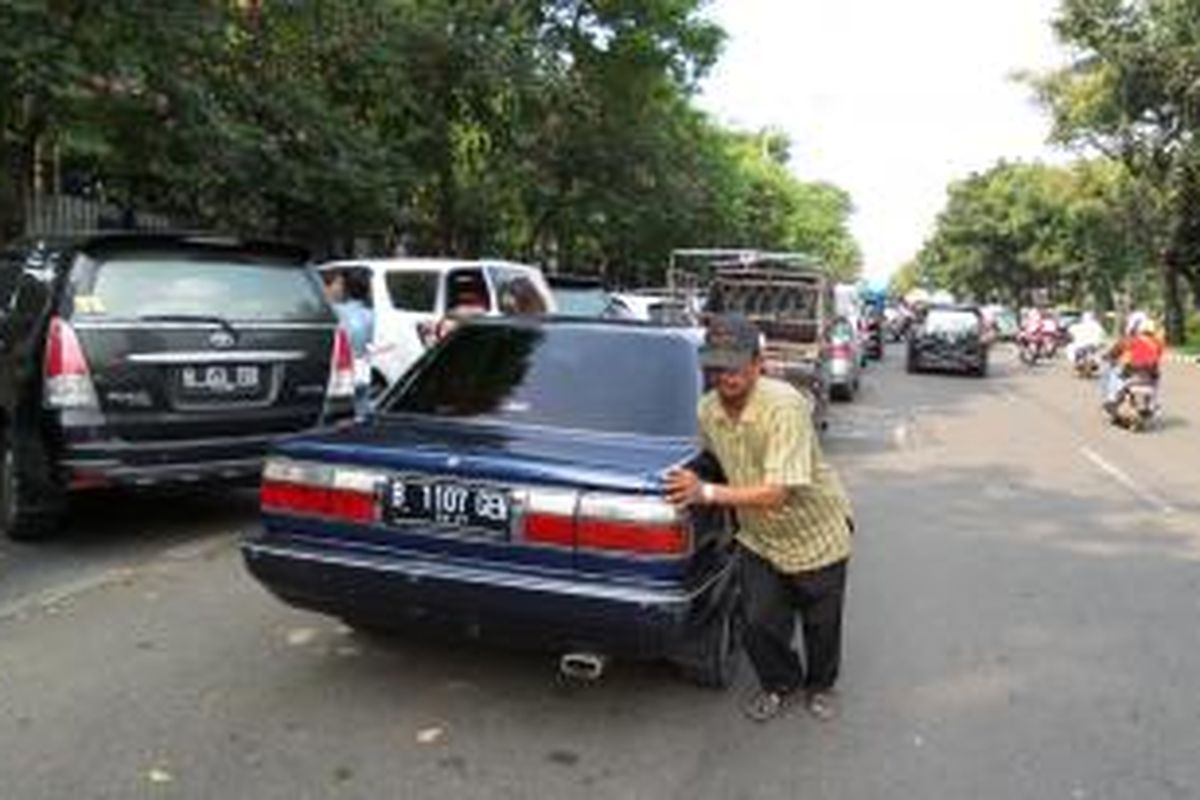 Seorang tukang parkir di Jalan Medan Merdeka Selatan, Jakarta, tengah mendorong mobil agar mobil lain bisa keluar, Kamis (31/7/2014). UP Perparkiran DKI Jakarta memastikan aktivitas mereka adalah ilegal.