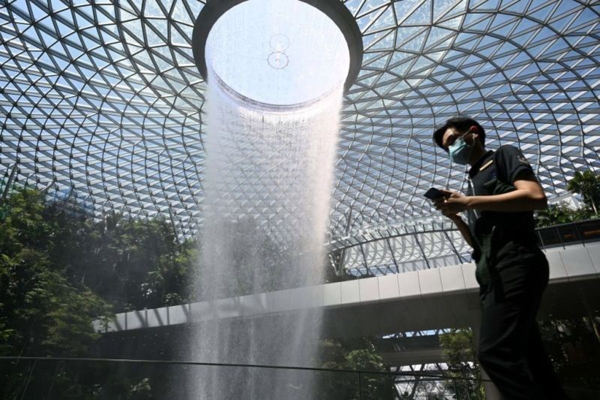 Seorang pengunjung terlihat memakai masker di depan objek wisata teranyar Singapura, air terjun Rain Vortex di Jewel Changi Airport. Air terjun dalam ruangan setinggi 40 meter ini diklaim merupakan yang terbesar di dunia.  