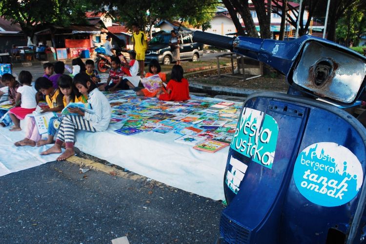 Anak-anak sedang membaca buku di kawasan Sebrang Pabayan, tepi Sungai Batang Arau, Padang, Sumatera Barat, Minggu (16/7/2017). Komunitas Baca Tanah Ombak meluncurkan kegiatan pustaka bergerak yang diberi nama Vespa Pustaka untuk menjangkau anak-anak di Kota Padang yang membutuhkan akses pendidikan lewat buku.