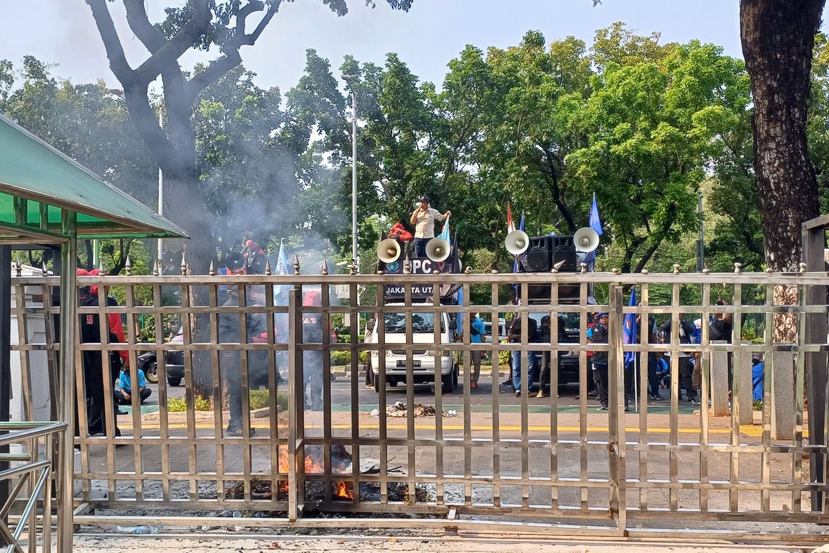 Massa buruh yang berdemonstrasi di depan Gedung Balai Kota DKI Jakarta membakar barang di Gerbang Masuk,  Selasa (21/11/2023).