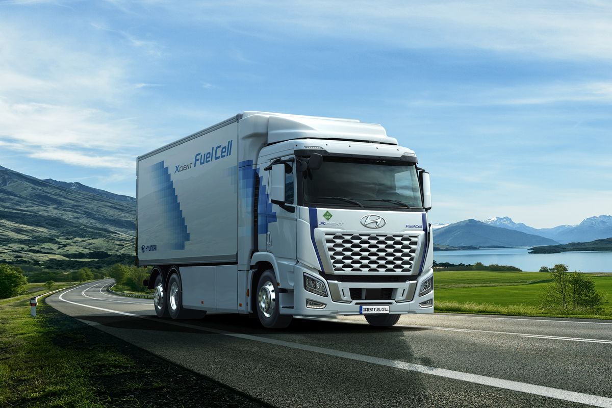 Truk Hyundai XCIENT White truck driving on the asphalt road next to the green field in rural landscape at sunset