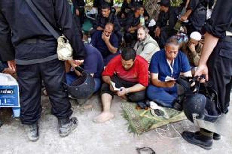 Polisi menjaga pendukung Presiden Mesir terguling Muhammad Mursi yang ditahan sambil membaca Al-Quran di kamp pengunjuk rasa dekat Universitas Kairo, Giza, Kairo, Mesir, 14 Agustus 2013.