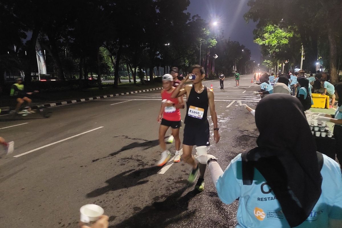 Pelari Kegiatan lomba lari maraton Lembaga Penjamin Simpanan (LPS) Monas Half Marathon 2023 saat memanfaatkan area air minum (water station) yang terletak di Jalan Medan Merdeka Selatan, Jakarta Pusat, Minggu (2/7/2023).