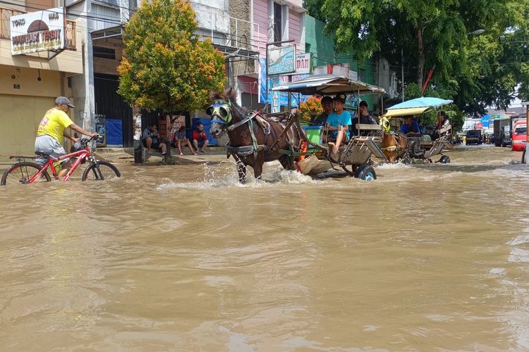 Kusir delman saat tengah mengantarkan penumpang melintasi banjir di Jalan Raya Dayeuhkolot, Kabupaten Bandung, Jawa Barat, Senin (31/11/2025) delman menjadi salah satu alternatif bagi warga dan pengendara yang tak berani menerjang banjir