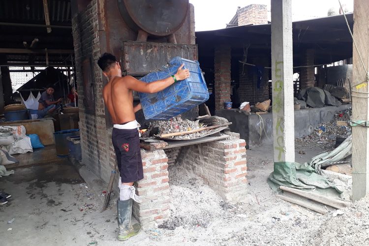 Pekerja pabrik tahu di Desa Tropodo, Kecamatan Krian, Sidoarjo, Jawa Timur, memasukkan limbah plastik impor sebagai bahan bakar pengganti kayu, Selasa (26/11/2019).