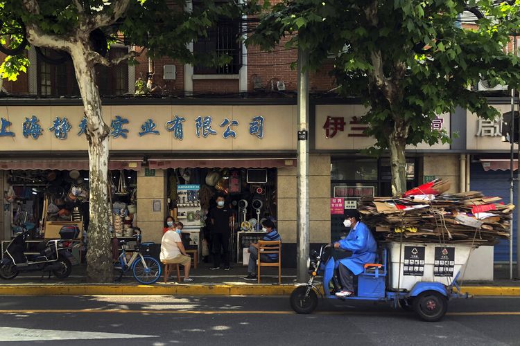 Seorang pekerja mengendarai gerobak penuh dengan kotak kertas yang lewat oleh penduduk di sebuah toko yang dibuka kembali setelah penguncian tindakan pandemi dicabut, Selasa, 31 Mei 2022, di Shanghai, China.