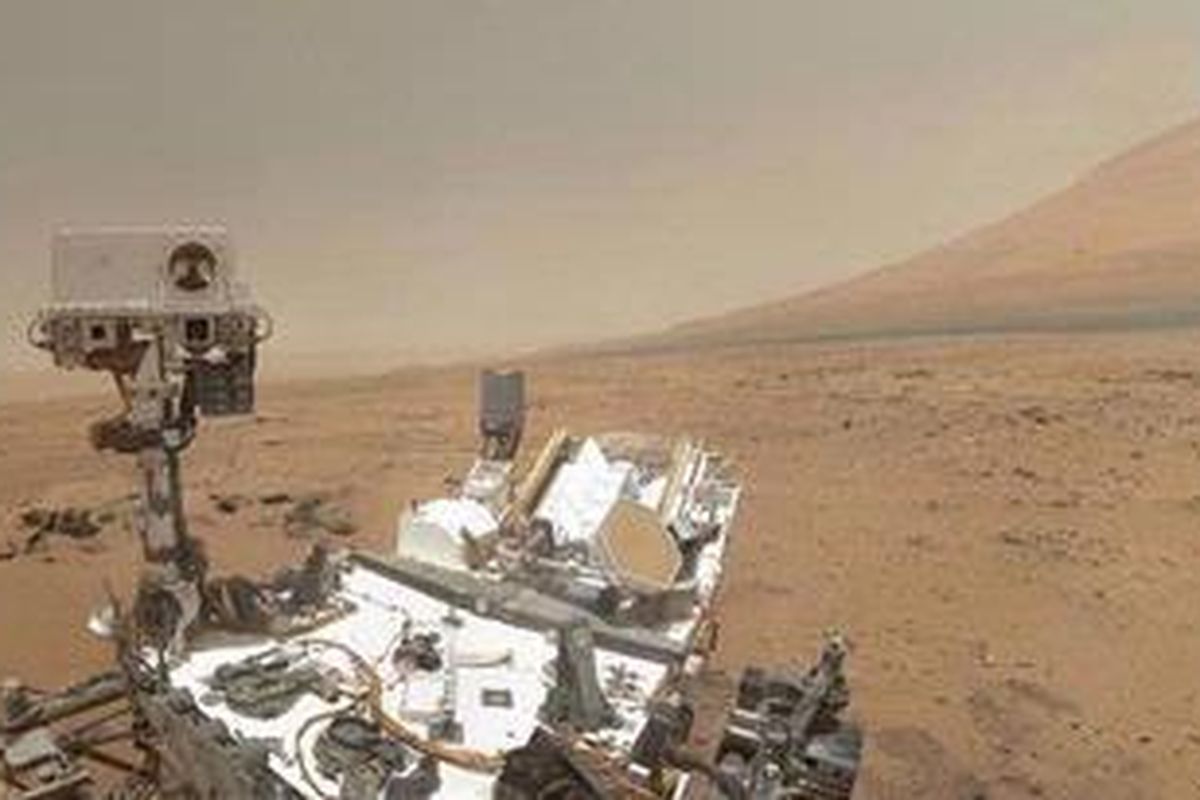 Potret Curiosity di Rocknest. Di sisi kanan Curiosity, terdapat Gunung Sharp yang menjulang setinggi 5 km dari Kawah Gale sebagai latar. 