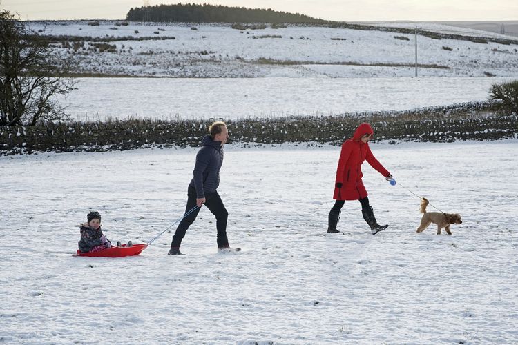 Natal, Jumat (25/12/2020) Sebuah keluarga sedang bermain di salju di gunung dekat Hexham, Inggris.