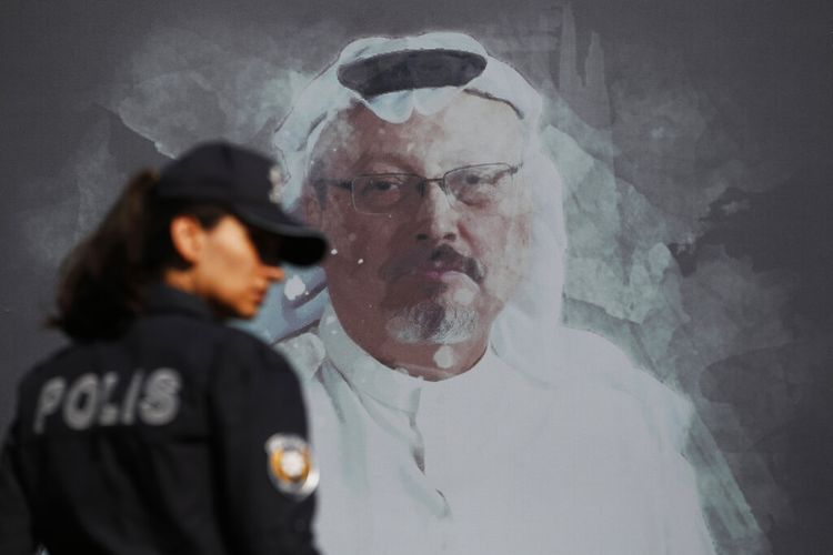 Seorang  polisi Turki berjalan melewati foto jurnalis Ara Saudi yang terbunuh, Jamal Khashoggi, sebelum upacara di dekat konsulat Arab Saudi di Istanbul, menandai peringatan satu tahun kematiannya .