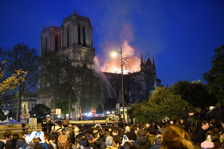 Kerumunan orang menyaksikan momen ketika api menjilat bagian atas Gereja Notre Dame di Paris, Perancis, pada Senin (15/4/2019). Belum diketahui penyebab pasti kebakaran itu.