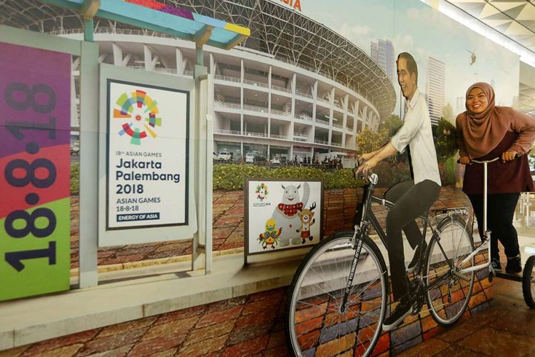 Seorang penumpang tengah berpose dengan foto Jokowi dan hiasan bertuliskan Asian Games 2018 di Terminal 3 Keberangkatan Bandara SOekarno-Hatta, Tangerang, Banten, Kamis (5/07/2018). PT Angkasa Pura AP (II) selaku pengelola bandara menyatakan siap memfasilitasi kedatangan dan kepulangan peserta Asian Games 2018 dengan menyiapkan sarana dan prasarana di tiga bandara yakni Bandara Soekarno Hatta, Bandara Sultan Mahmud Badaruddin II Palembang dan Husein Sastranegara Bandung.