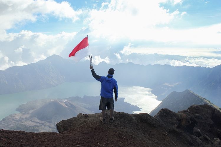 A photo illustrating a man with Indonesian flag standing on cliff at Mount Rinjani in West Nusa Tenggara province. 