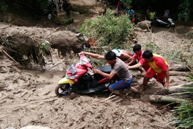 Seorang pengendara motor dibantu warga menyeberangi material longsor untuk menuju ke Kota Gorontalo.