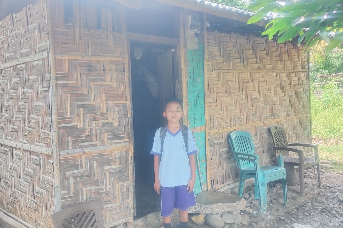 Glensius Okta Ombas (12) sedang berdiri di depan rumah Bapak Tuanya, Aloisius Patut, yang berdinding pelupuh bambu, saat pulang sekolah di Kampung Bugis, Kelurahan Ranaloba, Kecamatan Borong, Manggarai Timur, NTT, Jumat, (14/3/2025).