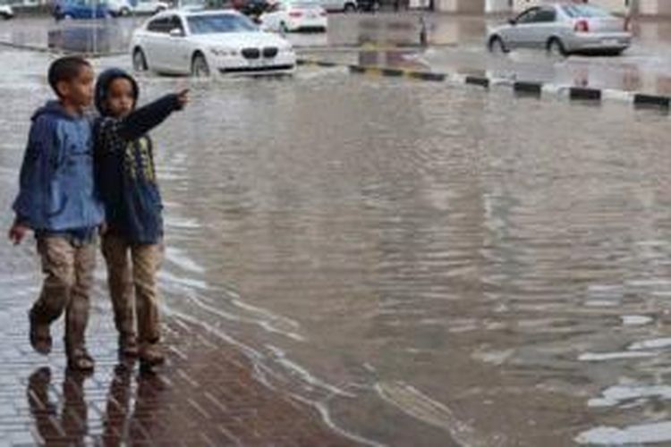 Dua orang bocah berjalan melintasi jalanan yang tergenang banjir akibat hujan deras di Sharjah, Uni Emirat Arab.