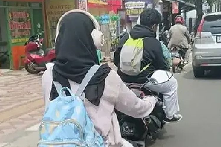 Foto pengendara motor ABG gunakan headphone tanpa pakai helm di jalan.