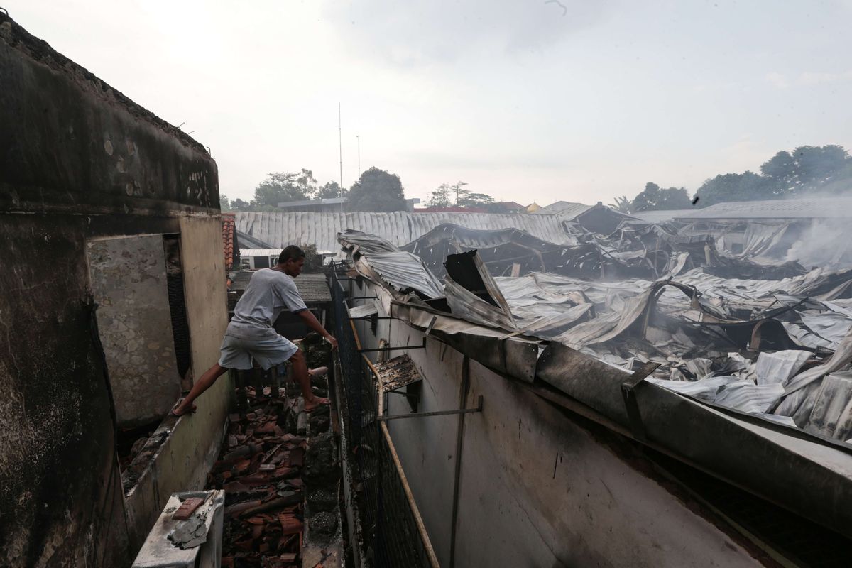 Warga melihat rumahnya yang ikut terbakar saat peristiwa  kebakaran melanda gudang JNE Express di Jalan Pekapuran, Cimanggis, Depok, Senin (12/9/2022). Kebakaran dilaporkan terjadi sekitar pukul 04.51 WIB, api berhasil dipadamkan sekitar pukul 08.57 WIB.