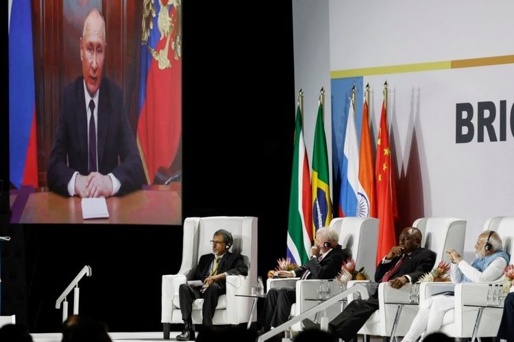 Presiden Rusia Vladimir Putin (tampak di layar monitor) memberikan pidato di KTT BRICS melalui rekaman video, Selasa (22/8/2023).