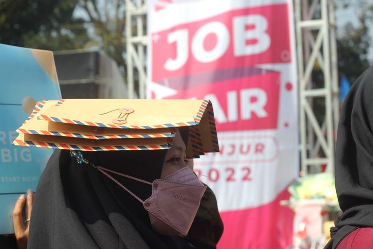 Melindungi kepalanya dari sengatan panas matahari dengan sejumlah berkas lamaran kerja, seorang pencari kerja (pencaker) mengantri di depan salah satu stan perusahaan di even Cianjur Job Fair 2022, Kamis (7/7/2022).