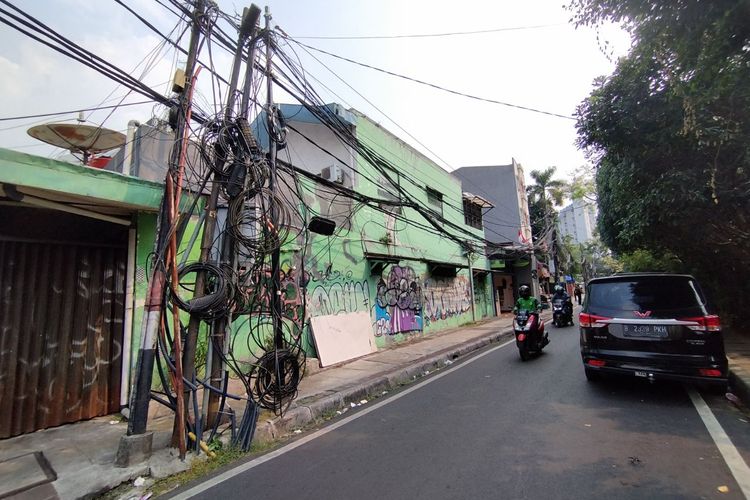 Tiang listrik miring dan kabel fiber optik menjuntai dan menggantung di Jalan Cikini IV, Menteng, Jakarta Pusat, Senin (7/8/2023).