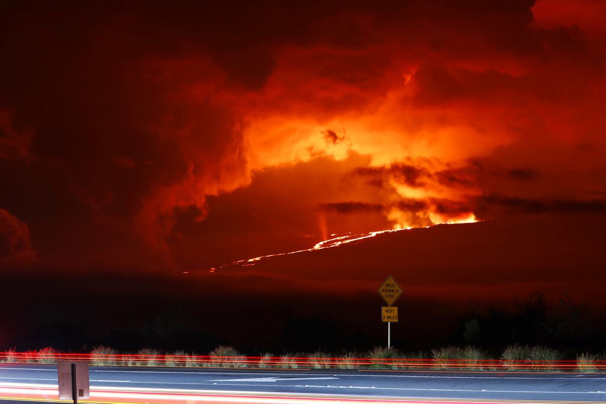 Dalam paparan kamera yang panjang ini, mobil berkendara di Saddle Road saat Mauna Loa meletus di kejauhan, Senin, 28 November 2022, dekat Hilo, Hawaii.