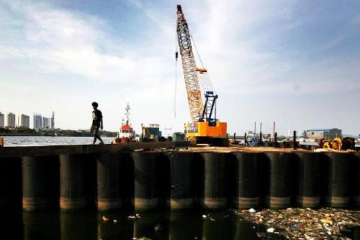 Warga melintas di antara dinding tabung raksasa yang dipasang sebagai bagian dari proyek pembangunan tanggul laut raksasa di Jakarta Utara, November 2014. 