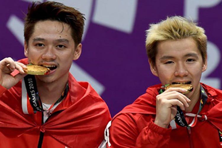 Pebulu tangkis ganda putra Indonesia Marcus F Gideon (kanan) dan Kevin Sanjaya (kiri) menggigit medali emas, usai upacara penyerahan medali bulu tangkis ganda putra Asian Games 2018 di Istora Senayan, Jakarta, Selasa (28/8). ANTARA FOTO/INASGOC/Puspa Perwitasari/tom/18.