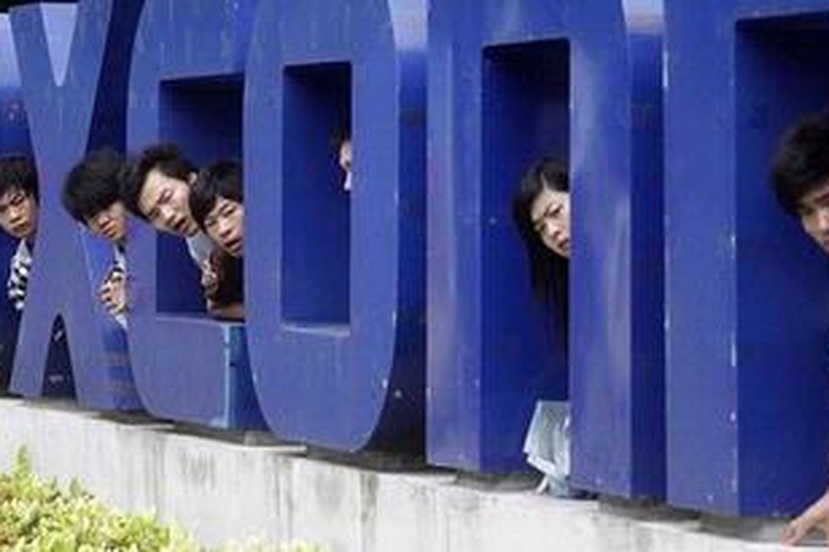No smiles: Workers look on from a Foxconn logo near the gate of a Foxconn factory in the township of Longhua, Guangdong province  